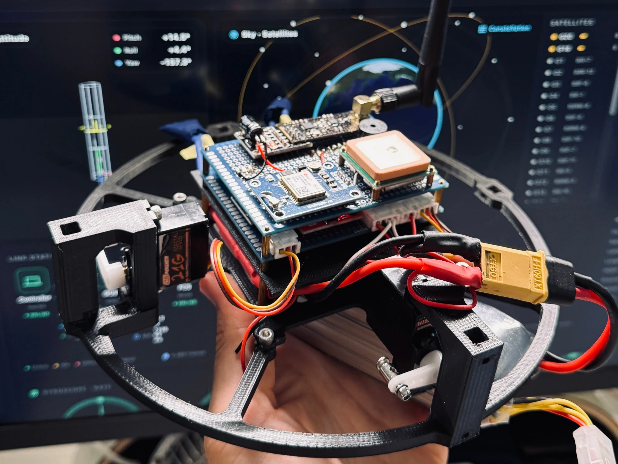 KAIROS with the cover off: the hand-wired board stack with GPS receiver, radio and gimbal servos, in front of the ground app
